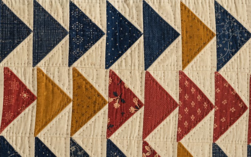Rows of flying-geese patchwork triangles in indigo, ochre and madder pointing across cream cotton.