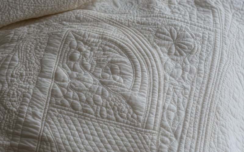 A detail of Provençal boutis: white-on-white corded wholecloth quilting with floral and geometric motifs raised in relief.